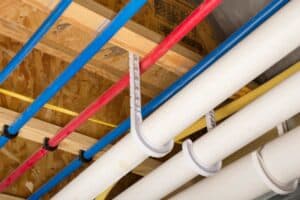 In Snellville, colored and white pipes are expertly installed under a wooden ceiling using sturdy plastic supports, ensuring your home re-pipe project is both efficient and reliable.