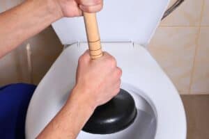 A person tackles a clogged toilet with a plunger, but it might be time to call for an emergency plumber in Madison.