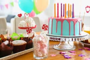 A colorful birthday cake with candles, surrounded by muffins, candy, and marshmallows on a table, creates the perfect centerpiece for the celebration. Balloons dance in the background like an emergency plumber in Madison arriving just in time to save the day.