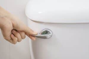 A hand reaches for the flush handle of a white toilet, signaling the first step in ensuring seamless toilet repair in Conyers.