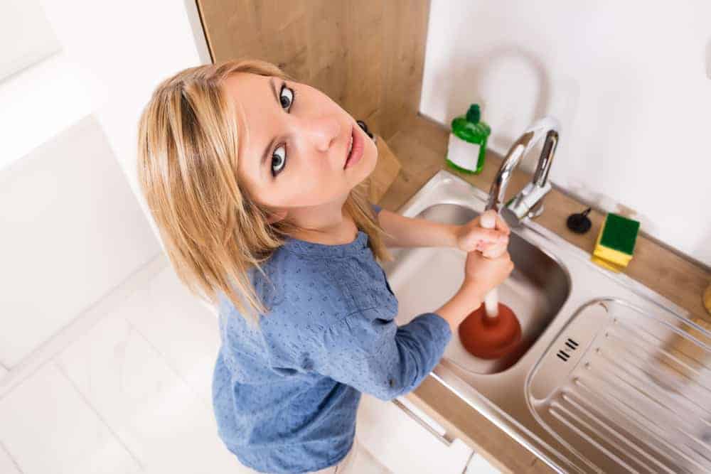 A young woman trying to fix a clog sink